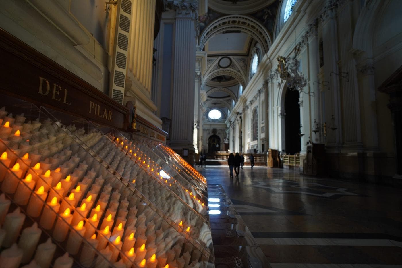 An ornate church interior featuring a row of glowing votive candles on the left.